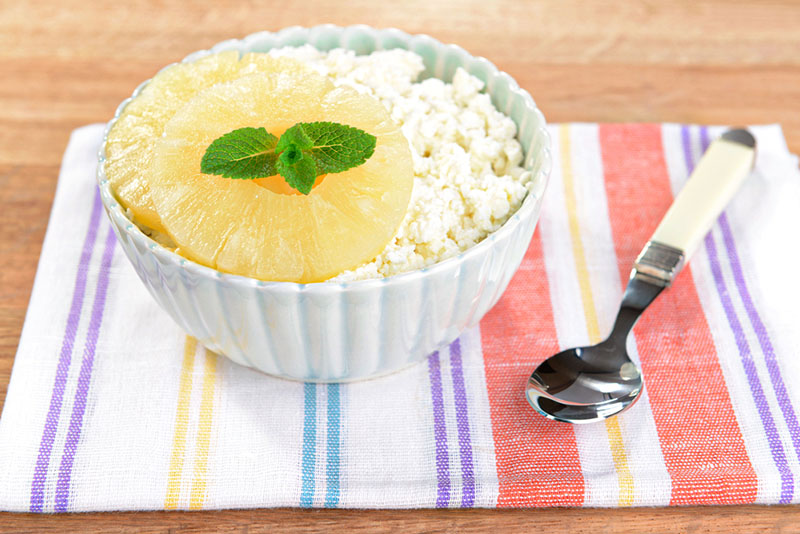 Bowl of tasty cottage cheese with pineapple on wooden table